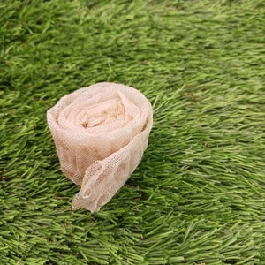 May include: A close-up of a beige, rolled-up piece of netting fabric on a green artificial grass surface.