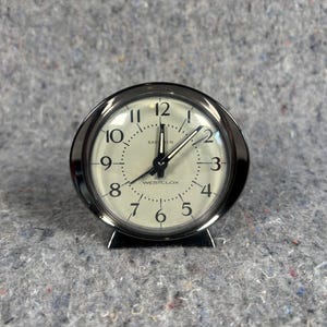 May include: A round Westclox Baby Ben alarm clock with a polished chrome metal frame and a cream-coloured face. The clock features black Arabic numerals, black hour and minute hands, a thin second hand, and the text Baby Ben and Westclox printed.