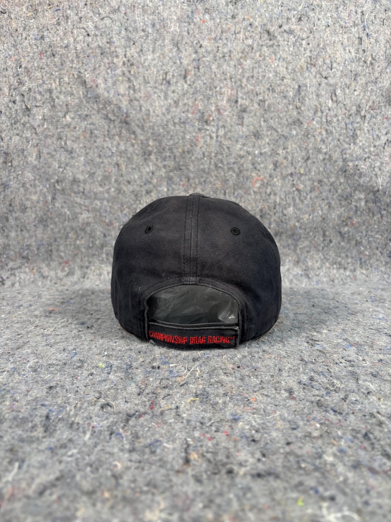 Puede incluir: Gorra de b&eacute;isbol negra con el texto "CHAMPIONSHIP UTAH RACING" en letras rojas. La gorra est&aacute; hecha de un material oscuro y texturizado y tiene una visera curva. La parte trasera de la gorra es visible, mostrando la correa ajustable.