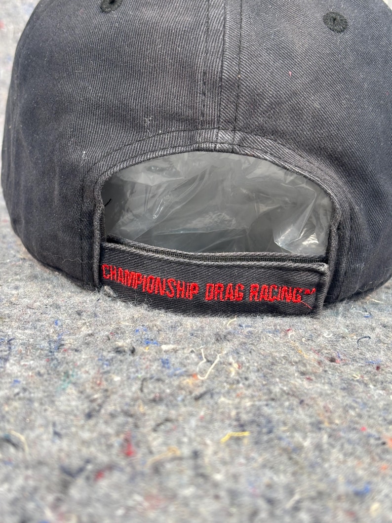 Puede incluir: Gorra de b&eacute;isbol negra con el texto "CHAMPIONSHIP DRAG RACING" bordado en rojo. La gorra tiene una visera curva y una correa de ajuste de pl&aacute;stico. Hecha de tela duradera.