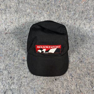 May include: Black cap with a curved brim and a rectangular patch. The patch features the text "MOLSON EXPORT" in white letters on a red background, with a white and black design.