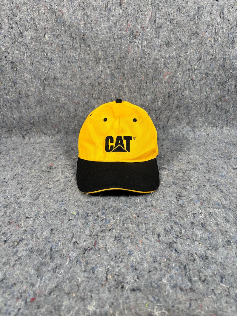 May include: Yellow and black baseball cap featuring the CAT logo in black. The cap has a yellow crown and a black peak. The CAT logo is displayed on the front.
