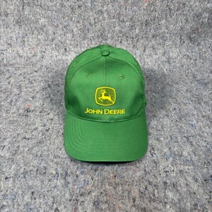 Könnte beinhalten: Grüne Baseballkappe mit gebogenem Schirm. Das gelbe Emblem zeigt ein Reh und den Schriftzug "JOHN DEERE". Die Kappe besteht aus strapazierfähigem Stoff und hat eine strukturierte Passform.