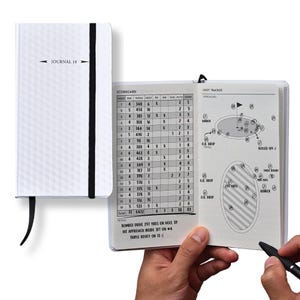 May include: White golf journal with the text "JOURNAL 18" and a black elastic closure. The journal is open to a scorecard and shot tracker, with a person holding a pen. The journal is designed for tracking golf scores and performance.
