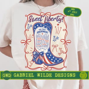 Può includere: T-shirt bianco con un design patriottico. Presenta uno stivale da cowboy rosso, bianco e blu, decorato con stelle e strisce. Il testo "Sweet Liberty!" e "The First Amendment" sono visualizzati. Include il testo "GWD GABRIEL WILDE DESIGNS".