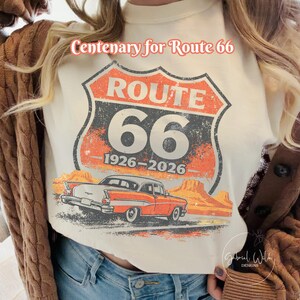 May include: Cream-colored Route 66 graphic tee. The design features the iconic Route 66 shield with "66" and "1926-2026" text, a vintage car, and desert scenery. The text "Centenary for Route 66" is above the graphic.