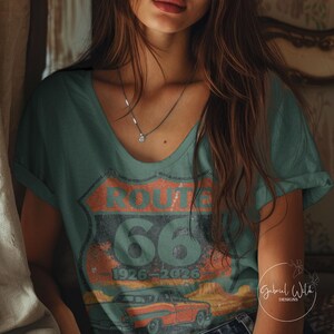 May include: Teal v-neck t-shirt featuring a distressed Route 66 graphic with the text "ROUTE 66" and "66" with the years "1926-2026". The graphic includes an illustration of a vintage car. The shirt is a casual wear item.