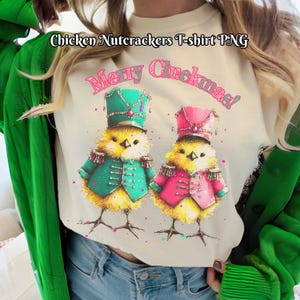 May include: Cream-colored t-shirt featuring two cartoon chicks dressed as toy soldiers, wearing teal and pink jackets and hats. The text "Merry Cluckmas!" is above the chicks. The text "Chicken Nutcrackers T-shirt PNG" is at the top.