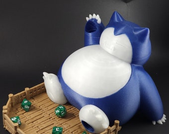 May include: A blue and white 3D printed Snorlax dice tower with a wooden fence base. Green dice are scattered on the wooden floor inside the tower.