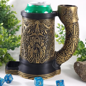 May include: A black and gold 3D printed can holder with a detailed design of a bearded man's face and intricate patterns. The holder has a built-in dice tray and a handle shaped like a dragon's head. Blue dice are scattered around the holder.