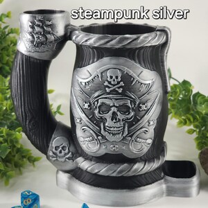 May include: Steampunk silver pirate skull dice tower with a wooden handle and a dice tray. The tower features a pirate skull with crossed swords and a skull and crossbones.