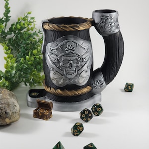 May include: A black and silver pirate-themed dice tower with a skull and crossbones design. The tower is made of wood and has a built-in dice tray. There are several green and gold dice scattered around the tower.