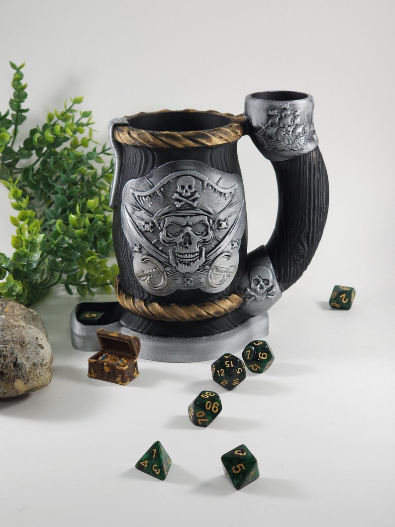 May include: A black and silver pirate-themed dice tower with a skull and crossbones design. The tower is made of wood and has a built-in dice tray. There are several green and gold dice scattered around the tower.