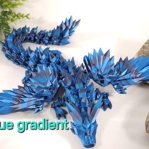 May include: A blue origami dragon with a gradient of color from dark blue to light blue. The dragon is made of paper and has a spiky, crystalline appearance. The dragon is posed with its wings spread out and its head tilted down.