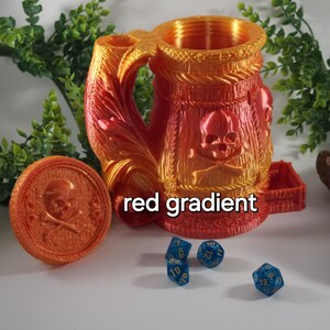 May include: A red and orange gradient 3D printed dice tower shaped like a skull-emblazoned mug with a lid and a removable tray. The tower is sitting on a white surface with blue dice.