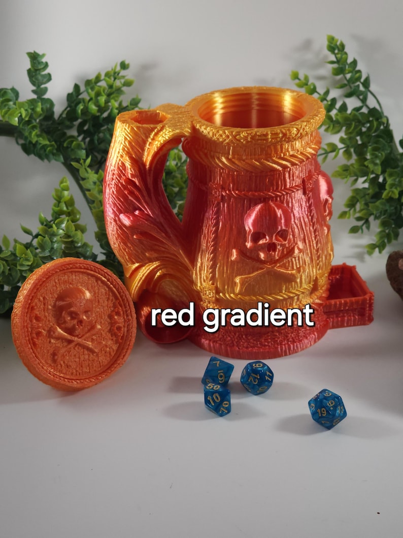 May include: A red and orange gradient 3D printed dice tower shaped like a skull-emblazoned mug with a lid and a removable tray. The tower is sitting on a white surface with blue dice.