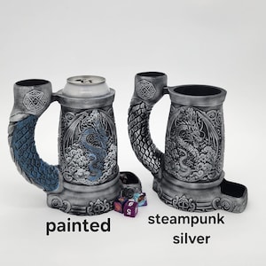 May include: Two silver-colored, dragon-themed beer steins. One has a blue dragon and handle, the other has a silver handle. The steins have a compartment for dice. The text "painted" and "steampunk silver" are below the steins.