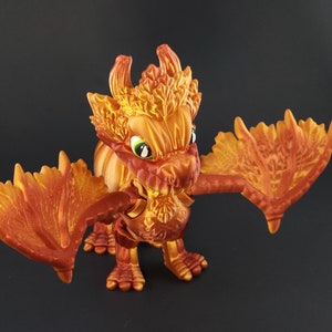 May include: A detailed figurine of a dragon with orange and yellow coloring. The dragon has large wings, a spiky head, and green eyes. The figure is standing on all fours with its wings spread out. The dragon's scales and features are highly detailed.