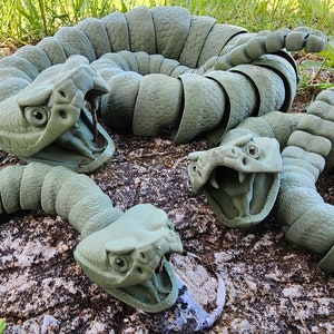 May include: A set of three green plastic snake sculptures. The snakes are segmented and have realistic details, including fangs and eyes. The snakes are arranged in a coiled position.