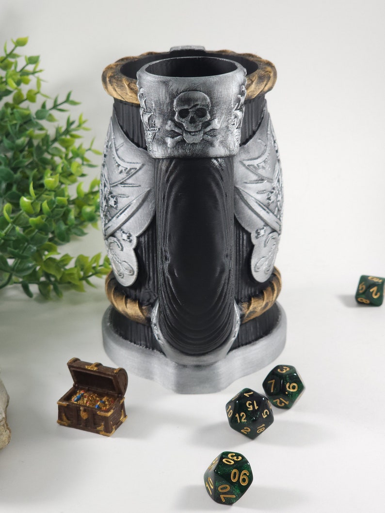 May include: A black and silver pirate-themed beer stein with a skull and crossbones design. The stein is surrounded by green dice and a small wooden treasure chest.