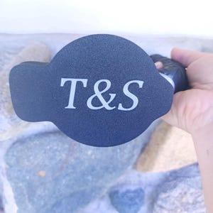 May include: Black round bottle stopper with a white inscription that reads "T&S".