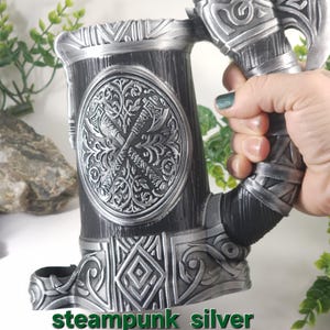 May include: Steampunk silver tankard with an axe handle and intricate details. The tankard is made of metal and has a wood-like texture. The text "steampunk silver no paint" is visible below the tankard.