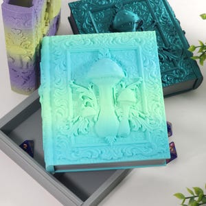 May include: A set of three decorative boxes shaped like books with a gradient color scheme. The boxes feature an ornate design with a mushroom motif. The boxes are open and reveal a gray interior.