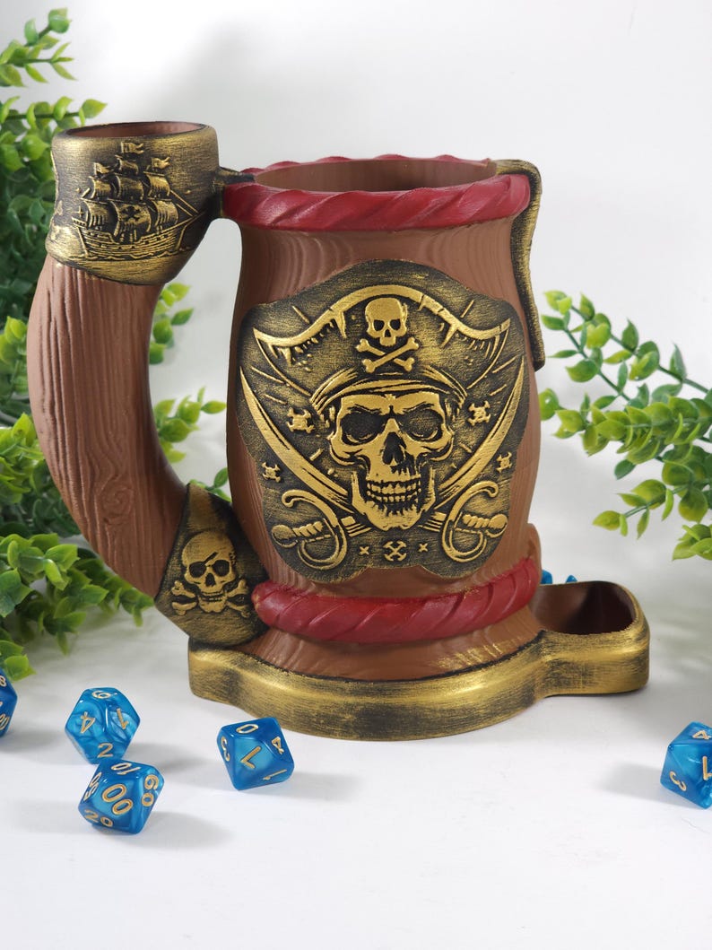 May include: A brown ceramic pirate-themed dice tower with a skull and crossbones design. The tower has a red rope detail and a gold trim. There are blue dice on the table in front of the tower.