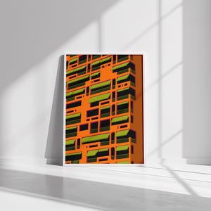 May include: Framed art print featuring a vibrant, geometric architectural design. The artwork showcases a repeating pattern of orange building facades with green and black window awnings. The print is displayed against a white wall and floor.