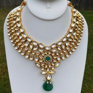 Peut inclure: Un collier en or avec un pendentif en pierre pr&eacute;cieuse verte. Le collier est compos&eacute; de petites pierres rondes serties d'or.
