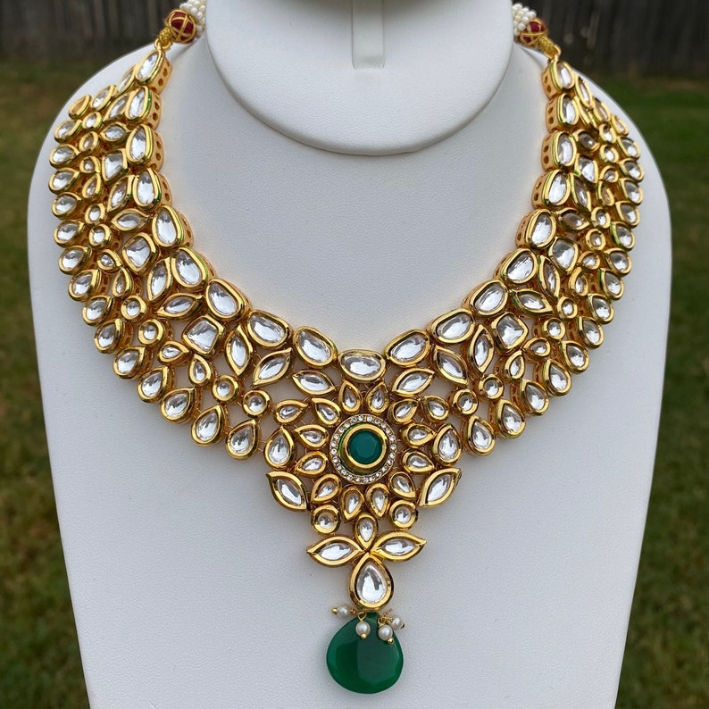 Peut inclure: Un collier en or avec un pendentif en pierre pr&eacute;cieuse verte. Le collier est compos&eacute; de petites pierres rondes serties d'or.