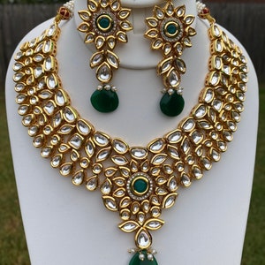 Peut inclure: Un collier et des boucles d'oreilles en or avec un pendentif en pierre verte et de nombreuses pierres claires. Le collier est un design superpos&eacute; avec un grand groupe de pierres en forme de fleur au centre.
