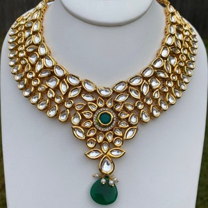 Peut inclure: Un collier en or avec un pendentif en forme de grosse pierre pr&eacute;cieuse verte. Le collier est compos&eacute; de petites pierres rondes et transparentes serties d'or.