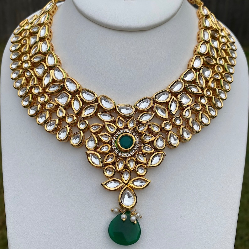 Peut inclure: Un collier en or avec un pendentif en forme de grosse pierre pr&eacute;cieuse verte. Le collier est compos&eacute; de petites pierres rondes et transparentes serties d'or.