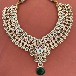Peut inclure: Un collier blanc, or et vert avec un pendentif en forme de larme. Le collier est compos&eacute; de petites pierres rondes serties d'or.