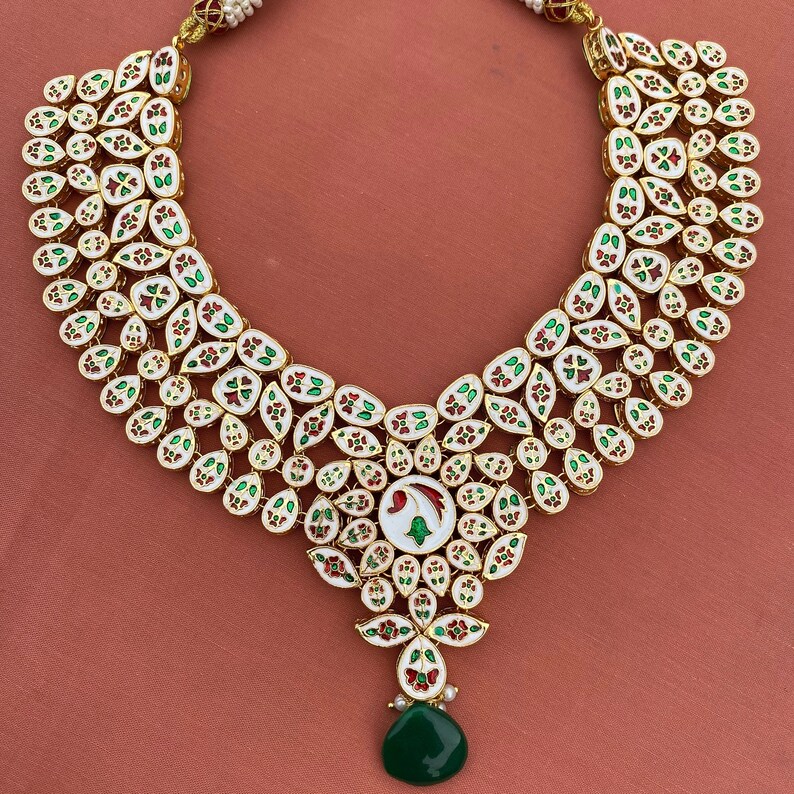 Peut inclure: Un collier blanc, or et vert avec un pendentif en forme de larme. Le collier est compos&eacute; de petites pierres rondes serties d'or.