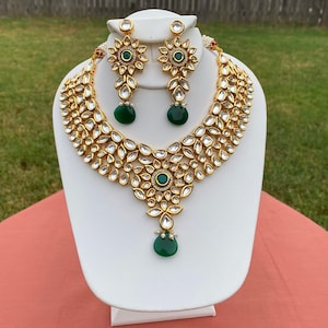 Peut inclure: Un collier et des boucles d'oreilles en or avec un pendentif en pierre verte et des pierres vertes sur les boucles d'oreilles. Le collier est compos&eacute; de petites pierres rondes et transparentes serties d'or.