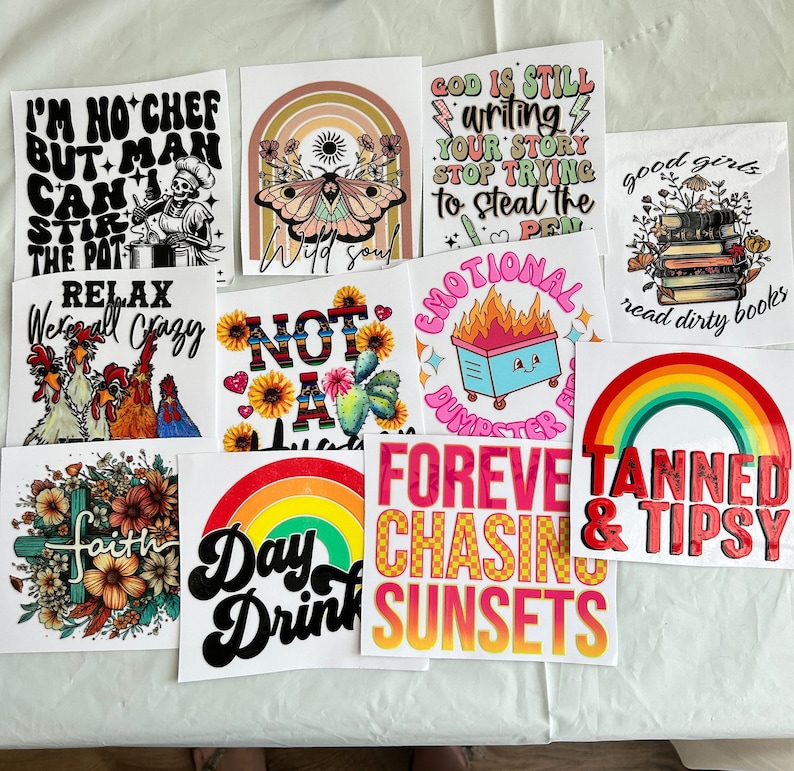 Puede incluir: Una colecci&oacute;n de pegatinas cuadradas con varios dise&ntilde;os y texto. Los dise&ntilde;os incluyen un chef esqueleto, una mariposa con un arco&iacute;ris, un fuego de basurero, una pila de libros, un arco&iacute;ris y frases como "Forever Chasing Sunsets" y "Tanned & Tipsy."