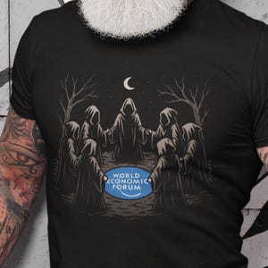 May include: Black t-shirt featuring a graphic of hooded figures under a crescent moon, with the text "WORLD ECONOMIC FORUM" on a blue circle. The shirt is worn by a person with tattoos and a white beard.