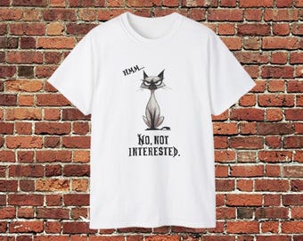 Puede incluir: Camiseta blanca con un diseño de gato de dibujos animados. El gato está representado con una expresión de mal humor, en tonos grises y negros. El texto de arriba dice "Hmm..." y debajo "No, Not Interested". El fondo es una pared de ladrillos rojos.