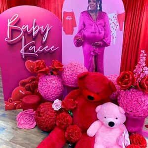 K&ouml;nnte beinhalten: Ein rosa-roter Babyparty-Hintergrund mit den Worten "Baby Kacee" in wei&szlig;er Schrift. Es gibt rosa und rote Blumen, einen gro&szlig;en roten Teddyb&auml;r und einen kleineren rosa Teddyb&auml;r.