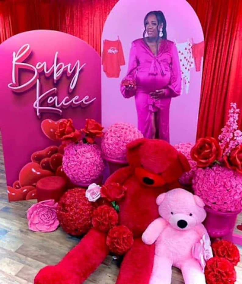 K&ouml;nnte beinhalten: Ein rosa-roter Babyparty-Hintergrund mit den Worten "Baby Kacee" in wei&szlig;er Schrift. Es gibt rosa und rote Blumen, einen gro&szlig;en roten Teddyb&auml;r und einen kleineren rosa Teddyb&auml;r.