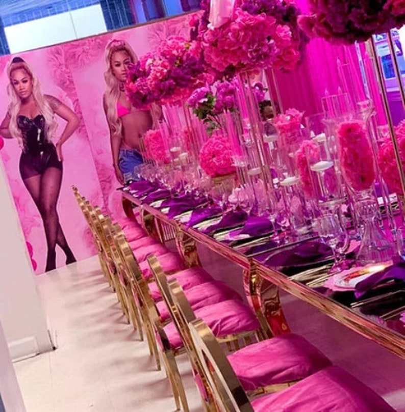 K&ouml;nnte beinhalten: Ein langer Tisch mit einer rosa Tischdecke und goldenen St&uuml;hlen ist f&uuml;r eine Party gedeckt. Der Tisch ist mit rosa Blumen und durchsichtigen Glasvasen dekoriert. Auf dem Tisch liegen rosa Servietten und durchsichtige Gl&auml;ser.