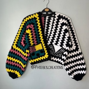 Op de afbeelding: Een gehaakt vest met een gespleten ontwerp. De linkerkant toont een kleurrijk granny square patroon in geel, groenblauw en roze. De rechterkant heeft een zwart-wit gestreept patroon met een wit driehoekig detail. @PHOEBES.CREATIONS
