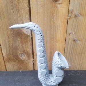 May include: A gray 3D printed saxophone with a textured surface and circular details.