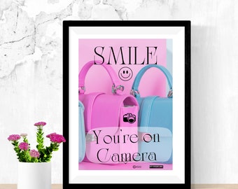 May include: A framed print with a pink background and the text "SMILE" with a smiley face. Three handbags are arranged in front of the text, one pink, one blue, and one with a camera graphic. The text "You're on Camera" is below the handbags.