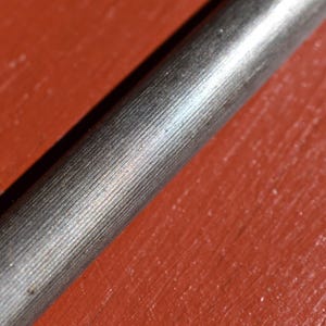 Pu&ograve; includere: Primo piano di un oggetto metallico con una superficie strutturata e rigata. L'oggetto &egrave; cilindrico e sembra essere realizzato in metallo color argento. Lo sfondo &egrave; di colore rosso-arancio uniforme.