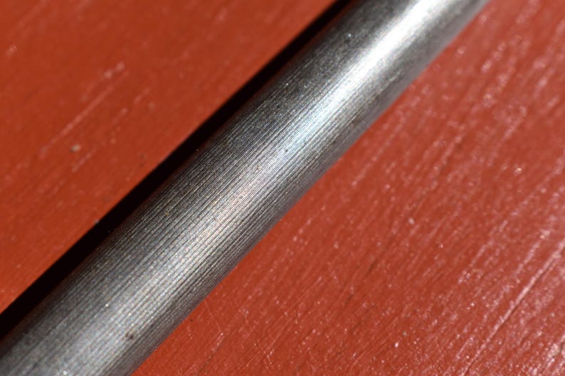 Pu&ograve; includere: Primo piano di un oggetto metallico con una superficie strutturata e rigata. L'oggetto &egrave; cilindrico e sembra essere realizzato in metallo color argento. Lo sfondo &egrave; di colore rosso-arancio uniforme.