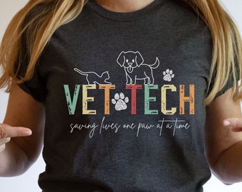 May include: Heather dark grey t-shirt with a retro-style graphic that says "VET TECH saving lives one paw at a time". The graphic features a cat and dog with paw prints.