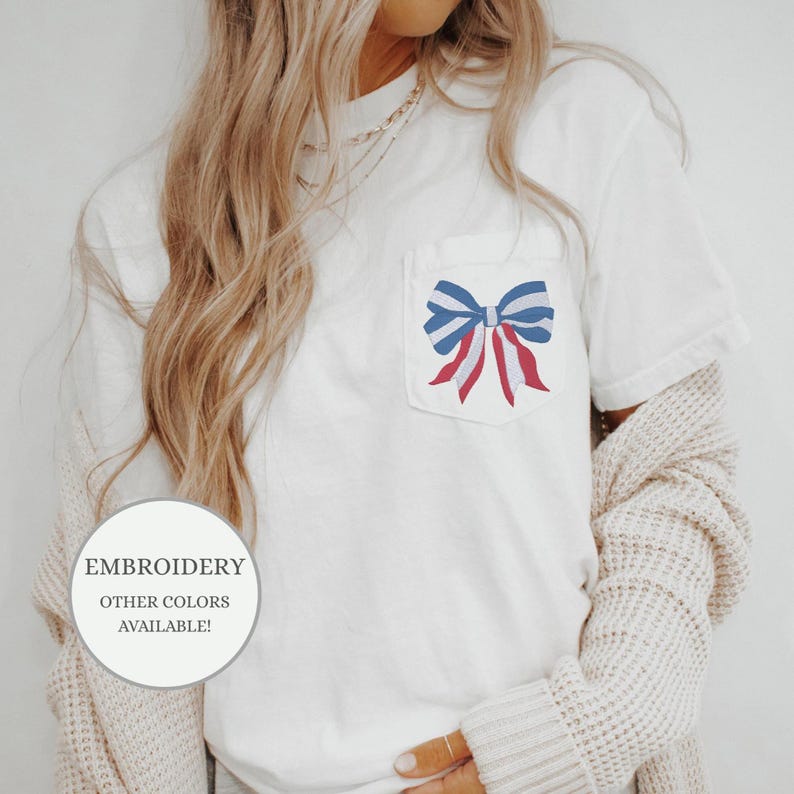 Pode incluir: Camiseta branca com um la&ccedil;o vermelho, branco e azul bordado em um bolso. O texto "EMBROIDERY OTHER COLORS AVAILABLE!" est&aacute; na parte inferior esquerda da imagem.